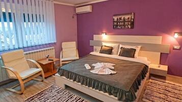 A bedroom with a bed, a chair, a nightstand, and a window with blinds.
