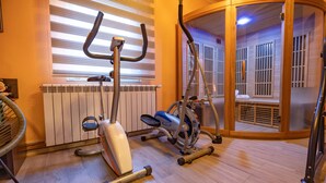 Un gimnasio con equipamiento de ejercicio, un radiador y una puerta de vidrio que da a una zona de sauna.