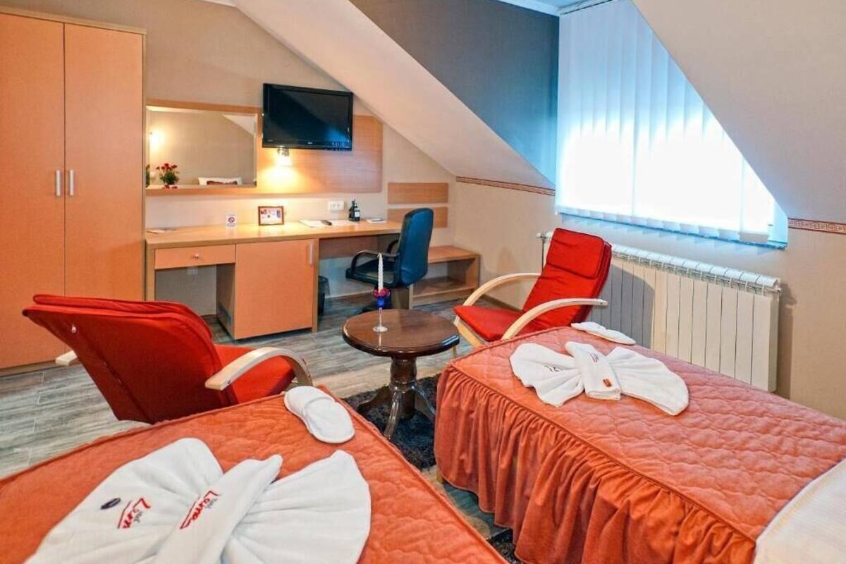 A hotel room with two beds, a desk, a chair, and a TV.