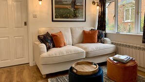 Een gezellige woonkamer met een witte bank, gestreepte kussens, een lijst met een foto en een raam met gordijnen.