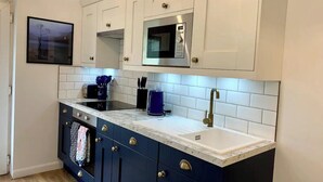 Een keuken met witte bovenkastjes, een magnetron, een spoelbak en een blauwe onderkast.