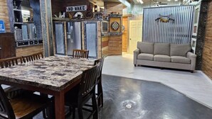A spacious living area with a dining table and chairs, a sofa, and a dartboard.