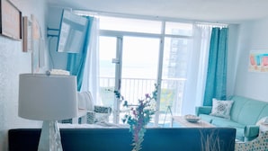 Ein Zimmer mit einem Holztisch, einer Lampe, einer Blumenvase, einer Seestern-Dekoration und Blick ins Freie durch ein Fenster.
