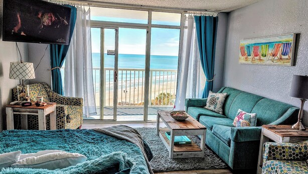 Ein Zimmer mit einem Bett, einem Schlafsofa, einem Fernseher, einem Tisch und Meerblick.
