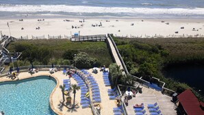 Ein Strandresort mit Schwimmbad, Liegestühlen und einer Mole, die zum Strand führt.