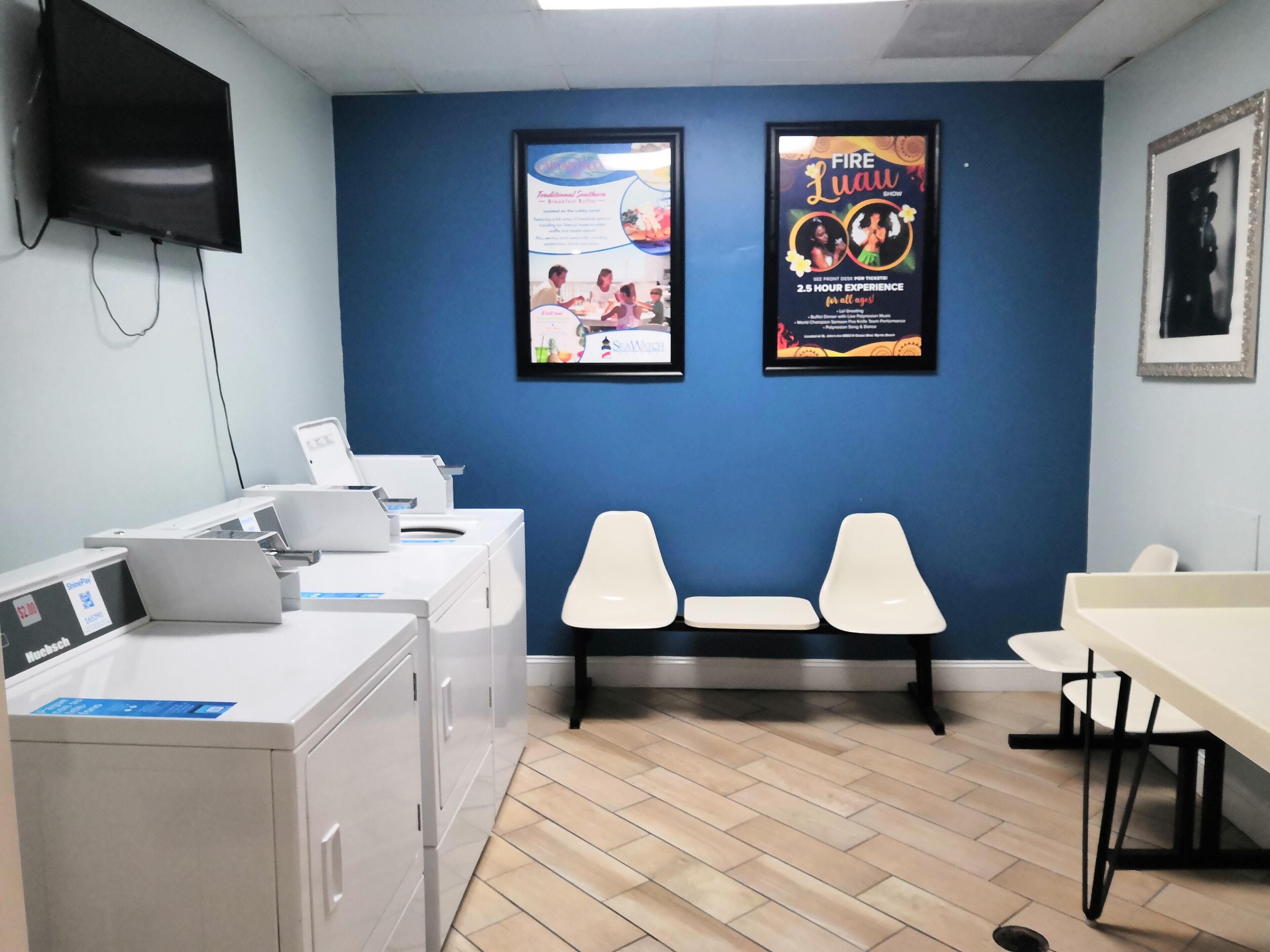 A room with a blue wall, a flat-screen TV mounted on the wall, a poster advertising a fire performance, and a table with chairs.