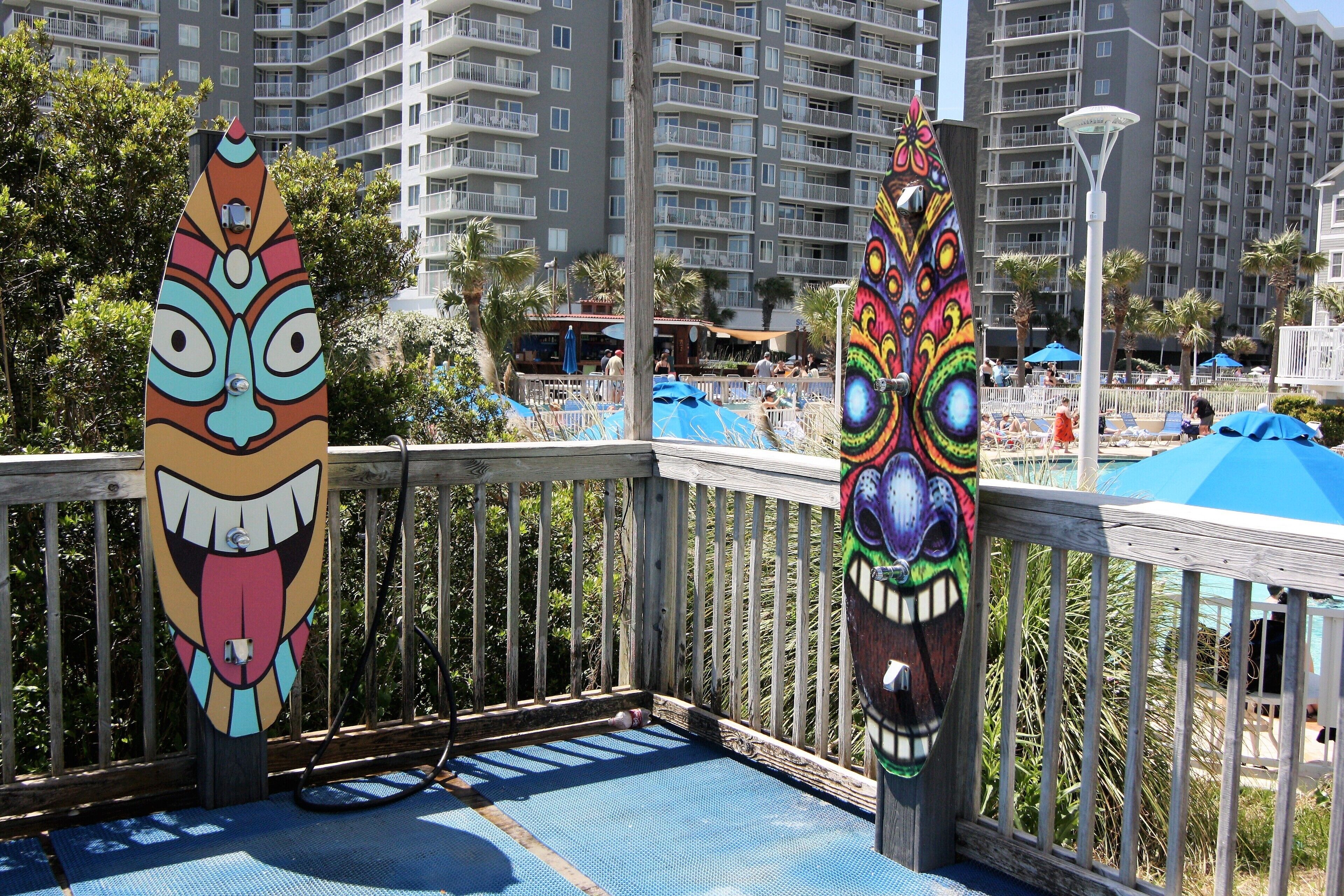 A wooden deck with two colorful surfboards and a view of a resort area with buildings and palm trees.