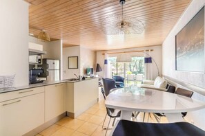 A modern kitchen with a dining area, featuring a wooden ceiling, a large window, and a view of the outdoors.