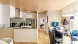 Een moderne keuken met een centraal eiland, een eethoek met een glazen tafel, en een zithoek met televisie.