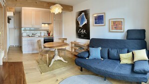A modern living room with a blue sofa, wooden dining table, and kitchen in the background. - Apartment (Fontainemelon)