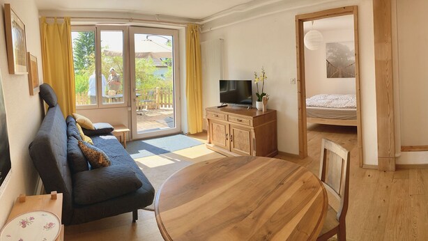 A cozy room with a sofa, a wooden dining table, a TV, and a bed. - Apartment (Fontainemelon)
