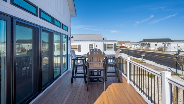 A wooden deck with a table and chairs, large windows, and a view of a street and other buildings. - Upscale Family Home for 10, Community Pool, Grill (Ocean City)