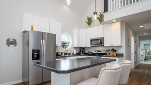 A modern kitchen with white cabinets, a stainless steel refrigerator, a microwave, and a central island with bar stools. - Upscale Family Home for 10, Community Pool, Grill (Ocean City)