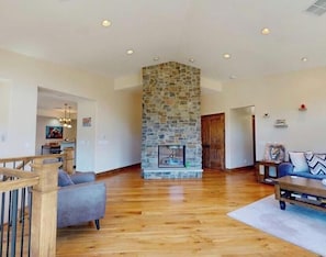 A spacious living area with a stone fireplace, wooden flooring, and a modern couch.