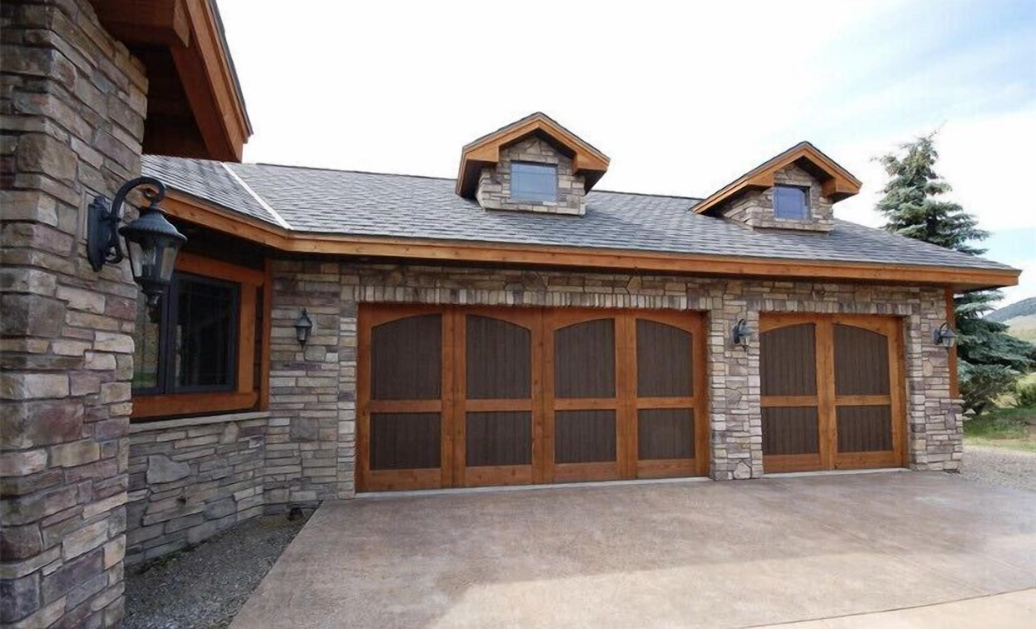 Un bâtiment en pierre avec un toit en pente, deux lucarnes et un grand garage doté de quatre portes.