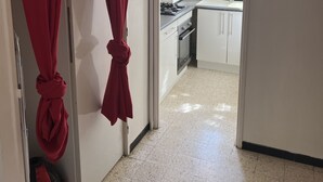 A hallway leading to a kitchen with white cabinets and a stove. Red curtains are tied at the top of the door frame. - Apartment near beach and shops (Argelès-sur-Mer)