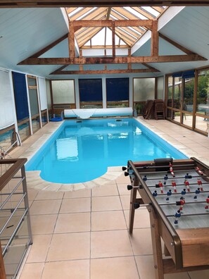 A swimming pool with a foosball table, a covered patio, and a view of the outdoors.