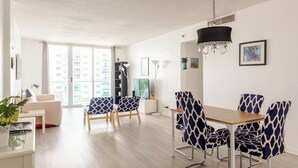 Un salon moderne avec un coin repas, de grandes fenêtres et une vue sur les immeubles.