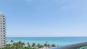 Une vue depuis un balcon donnant sur une plage bordée de palmiers, sous un ciel bleu et dégagé.