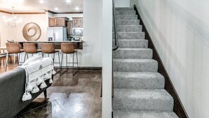 A modern kitchen with a dining area, a staircase, and a living room with a sofa.