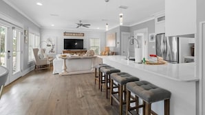 A modern kitchen with a central island, bar stools, and a large refrigerator. - GOLF CART - Heated POOL - 3 Kings/1 Queen - Walk to Beach - 5 Patios/Balconies! (Santa Rosa Beach)