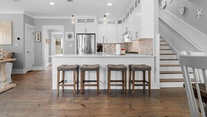 A modern kitchen with a central island, bar stools, and a staircase leading to a loft area. - GOLF CART - Heated POOL - 3 Kings/1 Queen - Walk to Beach - 5 Patios/Balconies! (Santa Rosa Beach)