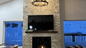 Una sala de estar moderna con chimenea de piedra, un televisor de pantalla plana montado y una lámpara de araña con cuernos únicos.