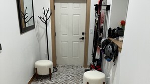 Un pasillo con suelo de espiga, una puerta blanca y un perchero con cascos y bolsas.
