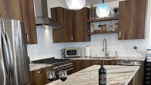 Una cocina moderna con una isla grande, electrodomésticos de acero inoxidable, gabinetes de madera e iluminación colgante.