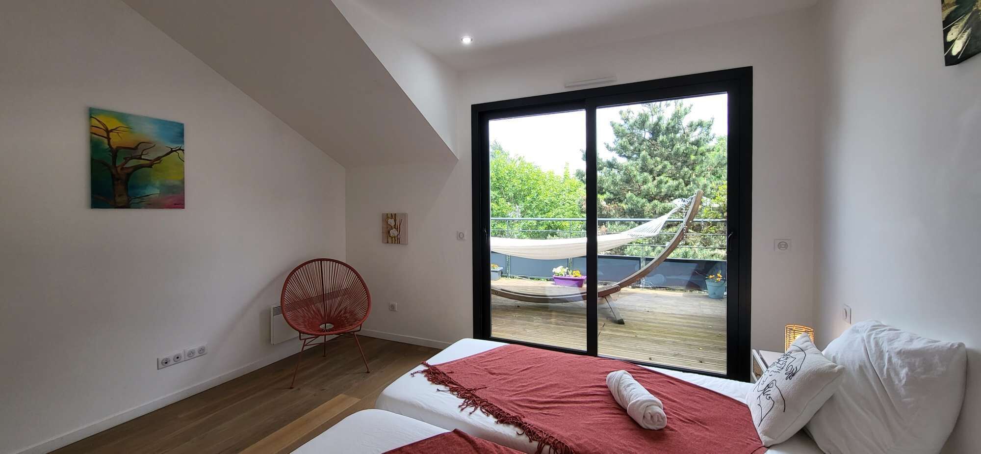 Camera da letto con un letto, un'amaca e un balcone vista verde.
