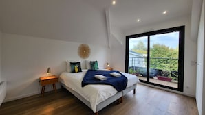 Un dormitorio moderno con una cama grande, una mesita de noche, una lámpara y vistas a un balcón con plantas.