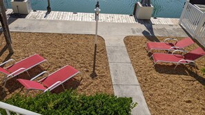 Un área junto a la piscina con sillas reclinables rojas y una terraza de madera.