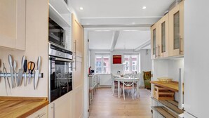 A modern kitchen with white cabinets, a built-in oven, and a dining area with a table and chairs.