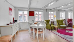 A spacious room with a dining table surrounded by chairs, a kitchen area, and a seating area with multiple chairs.