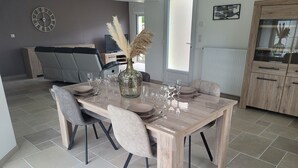 A dining area with a wooden table set for four, surrounded by chairs. A vase with pampas grass is on the table. - House located in a quiet cul-de-sac, close to the dunes. (Créances)