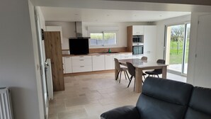 A modern kitchen with white cabinets, a built-in oven, and a large window. - House located in a quiet cul-de-sac, close to the dunes. (Créances)
