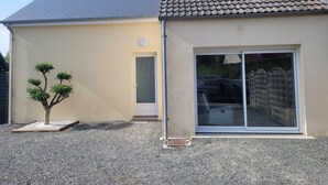 A building with a tiled roof, a small tree, and a sliding glass door. - House located in a quiet cul-de-sac, close to the dunes. (Créances)