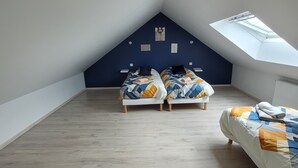 A room with a sloped ceiling, two beds with colorful bedding, a skylight, and a wooden floor. - House located in a quiet cul-de-sac, close to the dunes. (Créances)