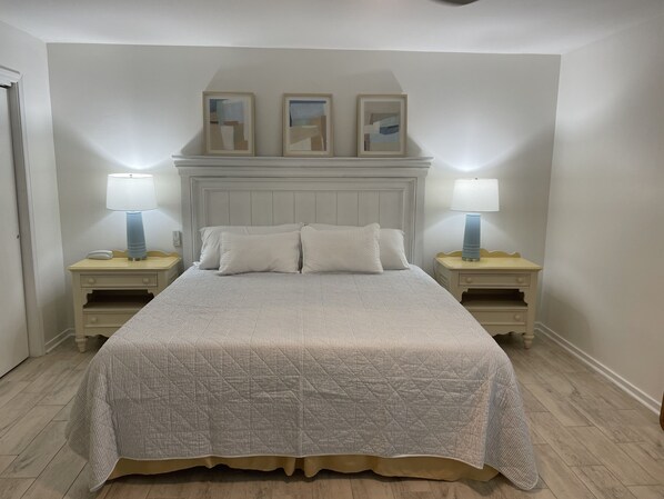 A neatly made bed with a quilted cover, two bedside tables with lamps, and three framed artworks above the bed.