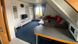 A cozy, well-lit room with a television, seating area, and a dining table. - Vacation apartment Assing am Deich (Dornum)