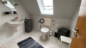 A small, modern bathroom with a skylight, a sink, a toilet, and a shower area. - Vacation apartment Assing am Deich (Dornum)
