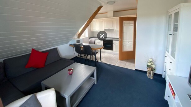 A compact living space with a sofa, a coffee table, a dining area with chairs, and a kitchenette. - Vacation apartment Assing am Deich (Dornum)
