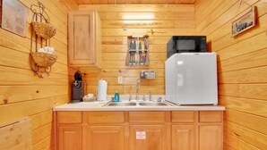Eine kleine Küche mit Holzausstattung, einem weißen Kühlschrank, einer Mikrowelle und einem Spülbecken.