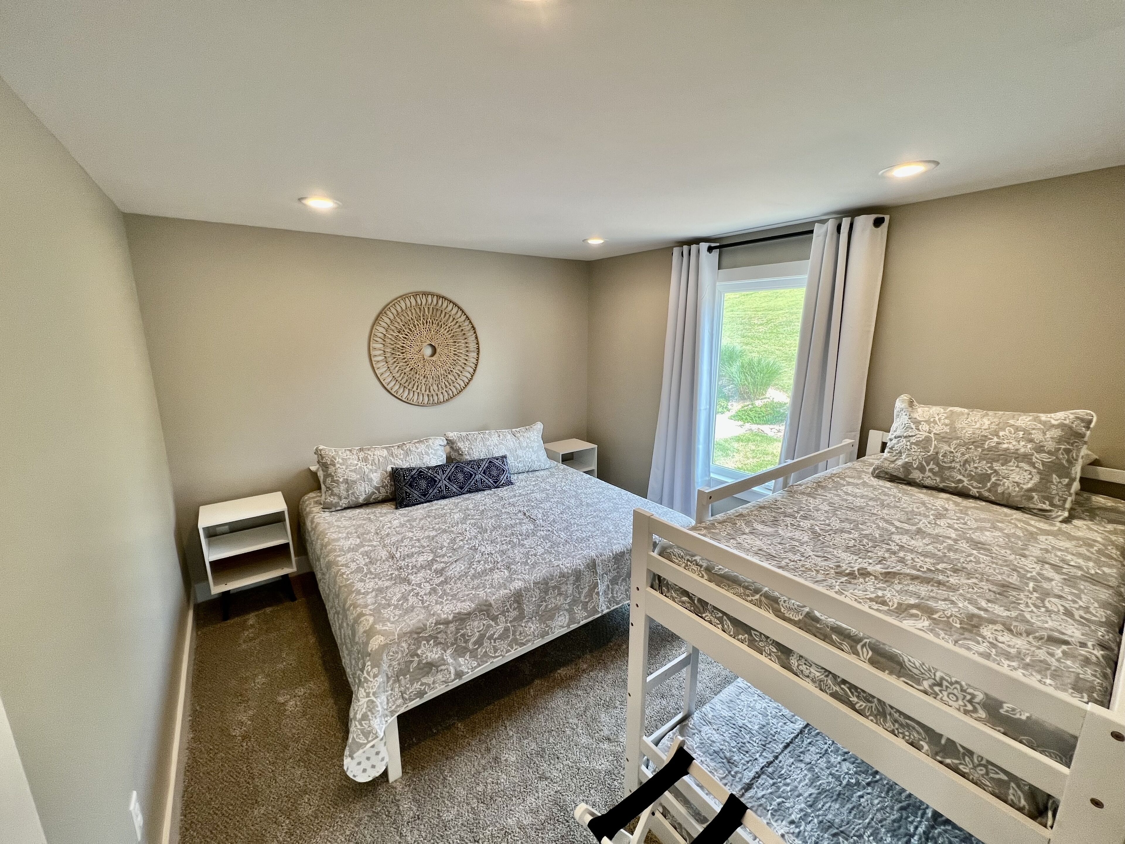 A bedroom with two beds, a decorative wall piece, a window with curtains, and a carpeted floor.