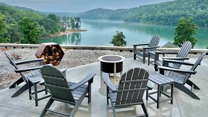 An outdoor seating area with Adirondack chairs and a round table, overlooking a lake and forested hills. - Modern Lake Cottage - Amazing Views - 6 Bed/6 Bath - Boat Launch (LaFollette)