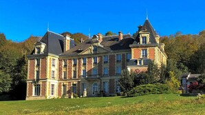 A large, historic building with multiple stories, prominent architectural details, and a well-maintained surrounding lawn.