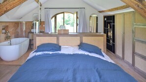 A bedroom with a large bed, a bathtub, and a wooden ceiling.