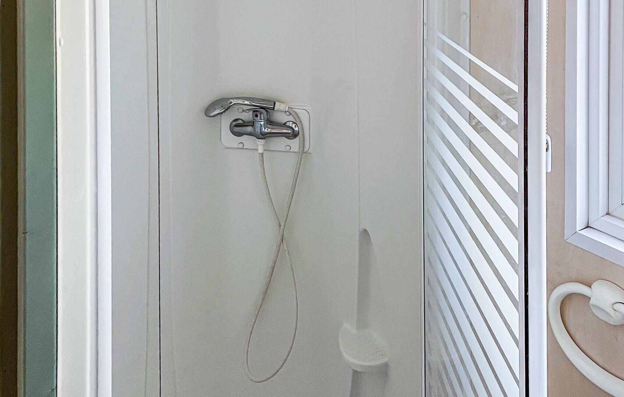 Une douche équipée d’un pommeau de douche à main et d’un robinet fixé au mur.