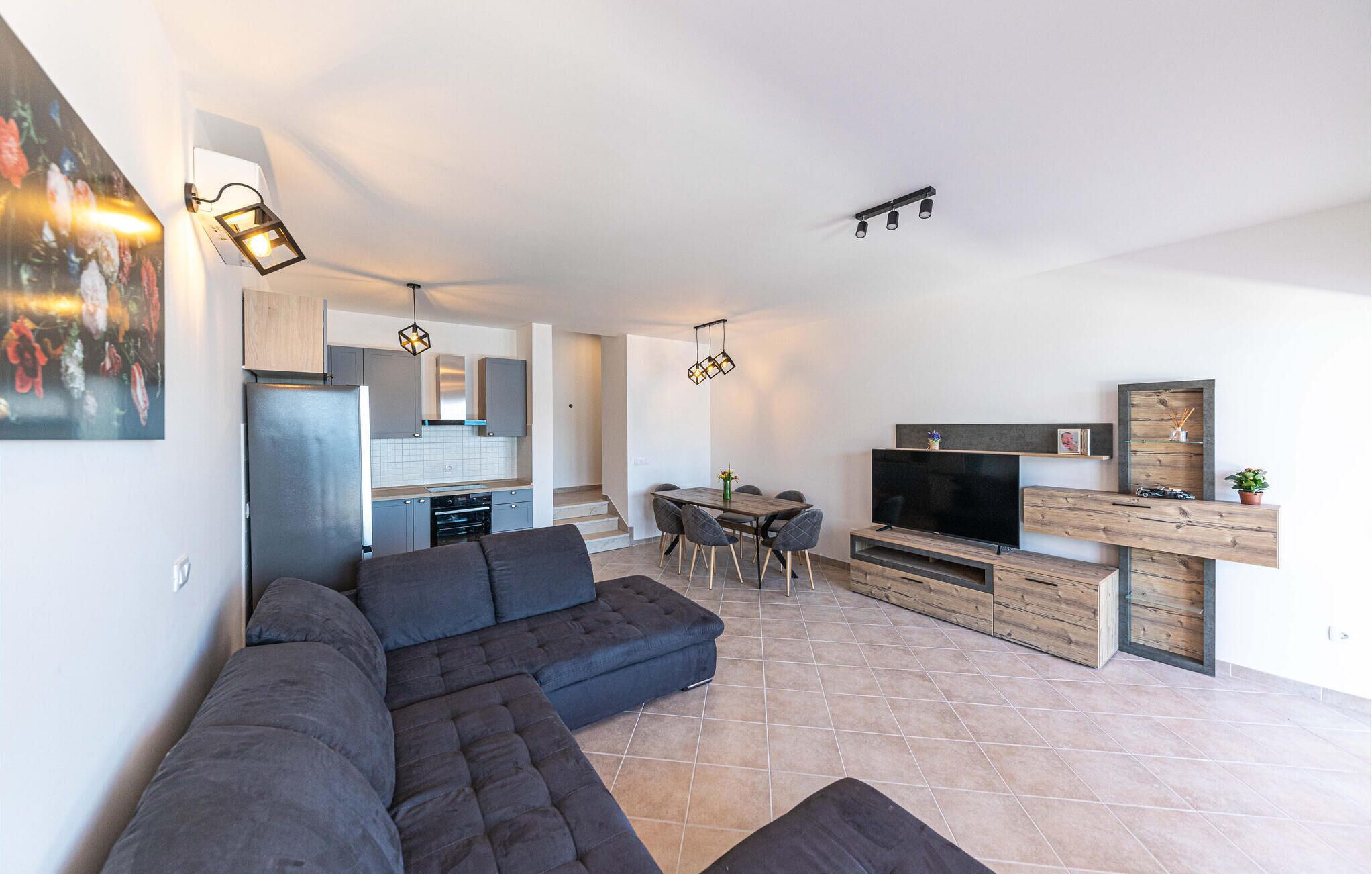 Una sala moderna con un sofá seccional, un comedor con televisor y una cocina con refrigerador y armarios.