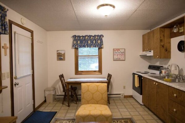 A compact kitchen with a dining table, chairs, a window with a patterned valance, and a kitchen counter with cabinets.